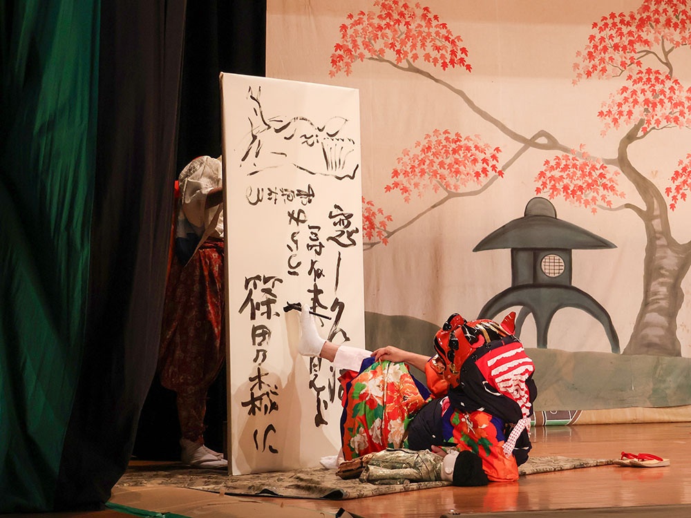 獅子頭をかぶった役者がふすまに足を使って文字を書く