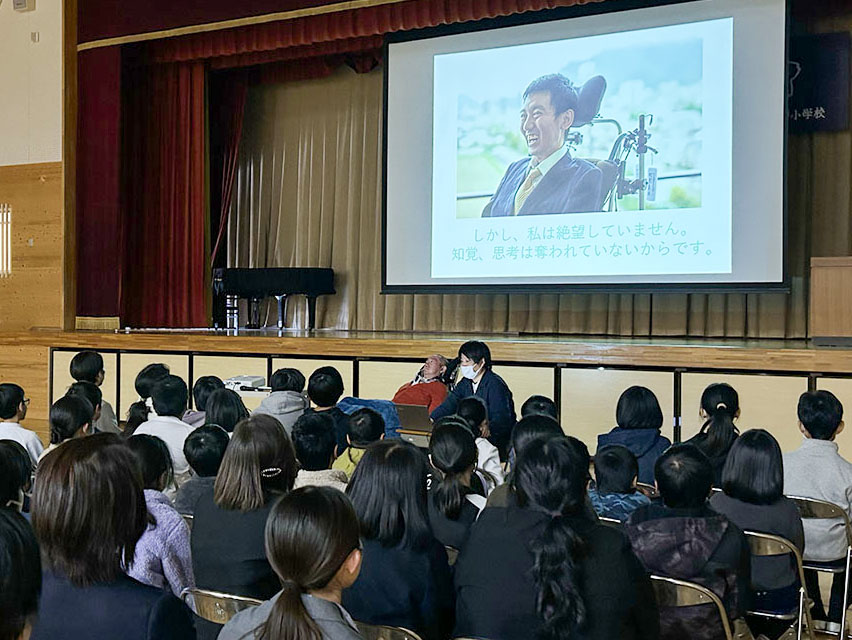 スライドと合成音声で講演をする恩田さんと、聞く児童ら