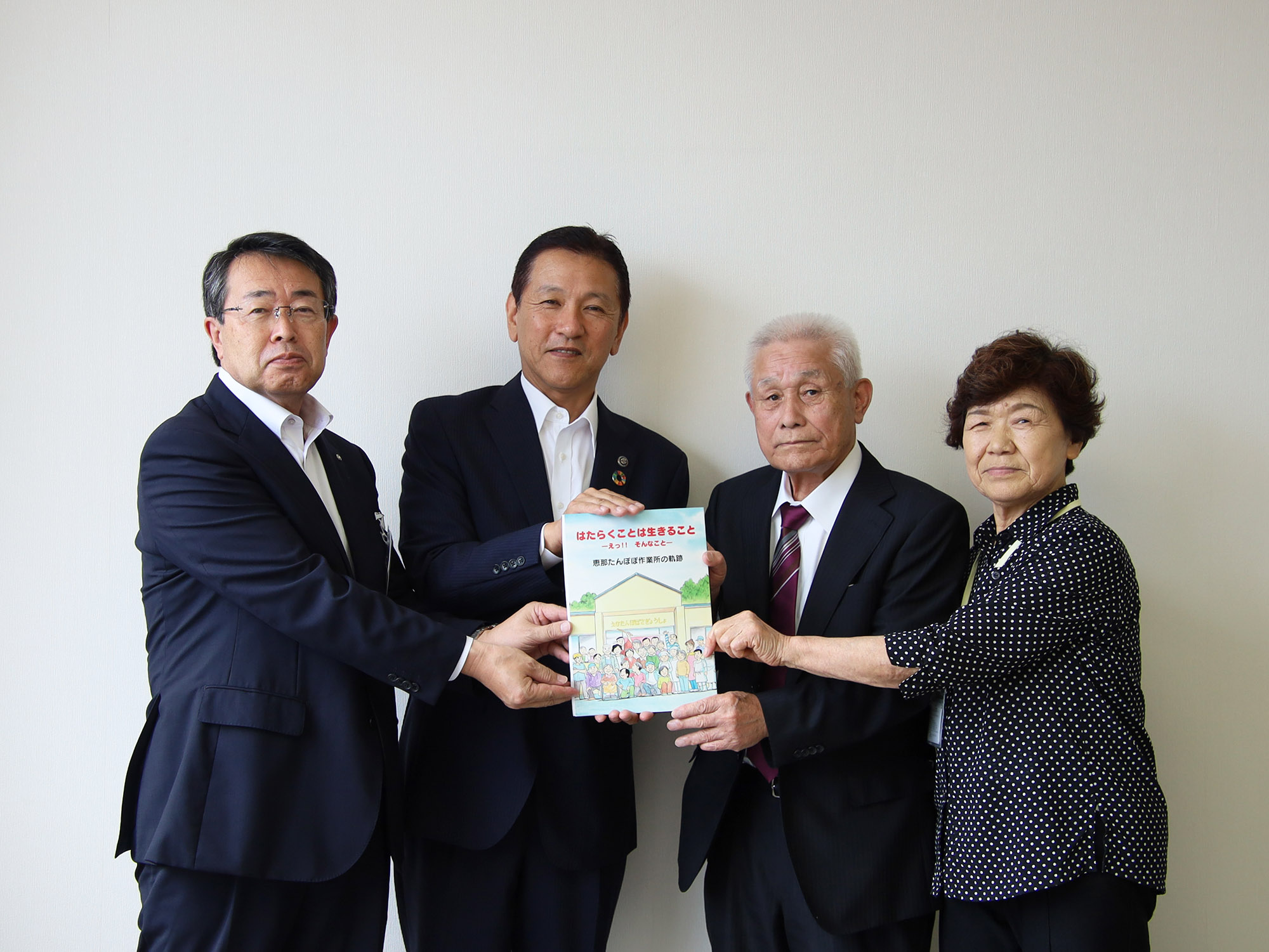たんぽぽ福祉会の小板理事長と遠山総合施設長から 漫画『はたらくことは生きること』を受け取る小坂市長と岡田教育長