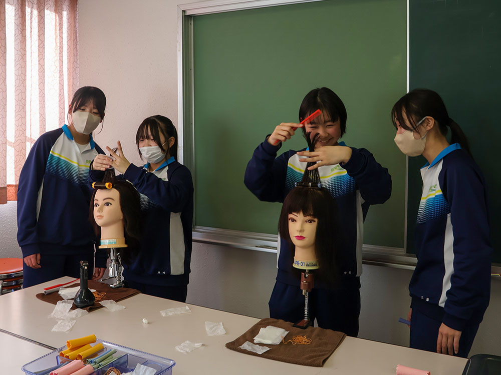 美容院のブースで、パーマを巻く体験をする中学生ら