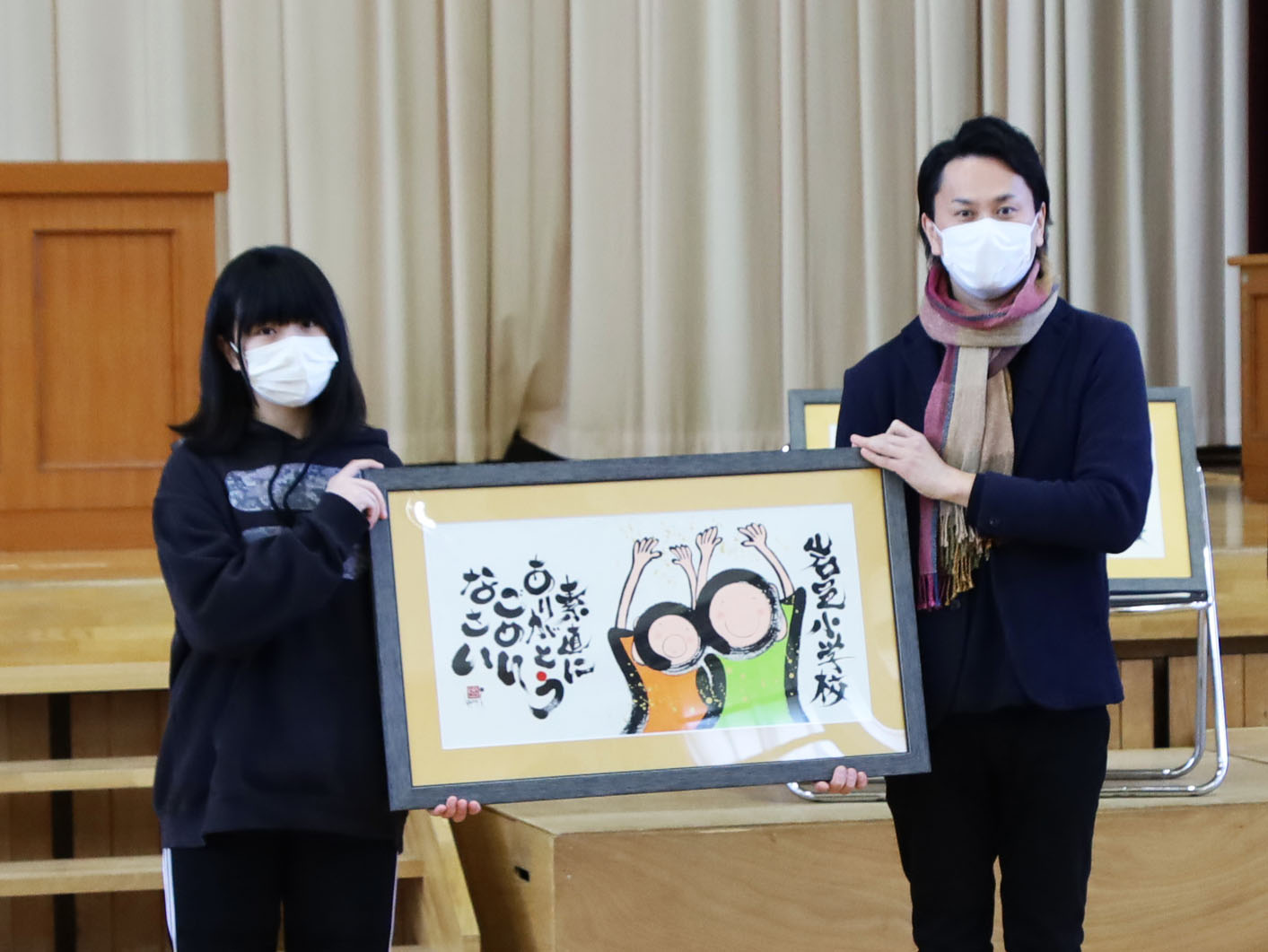 伊藤さんから書画を受け取る児童委員長の伊藤菜乃夏さん