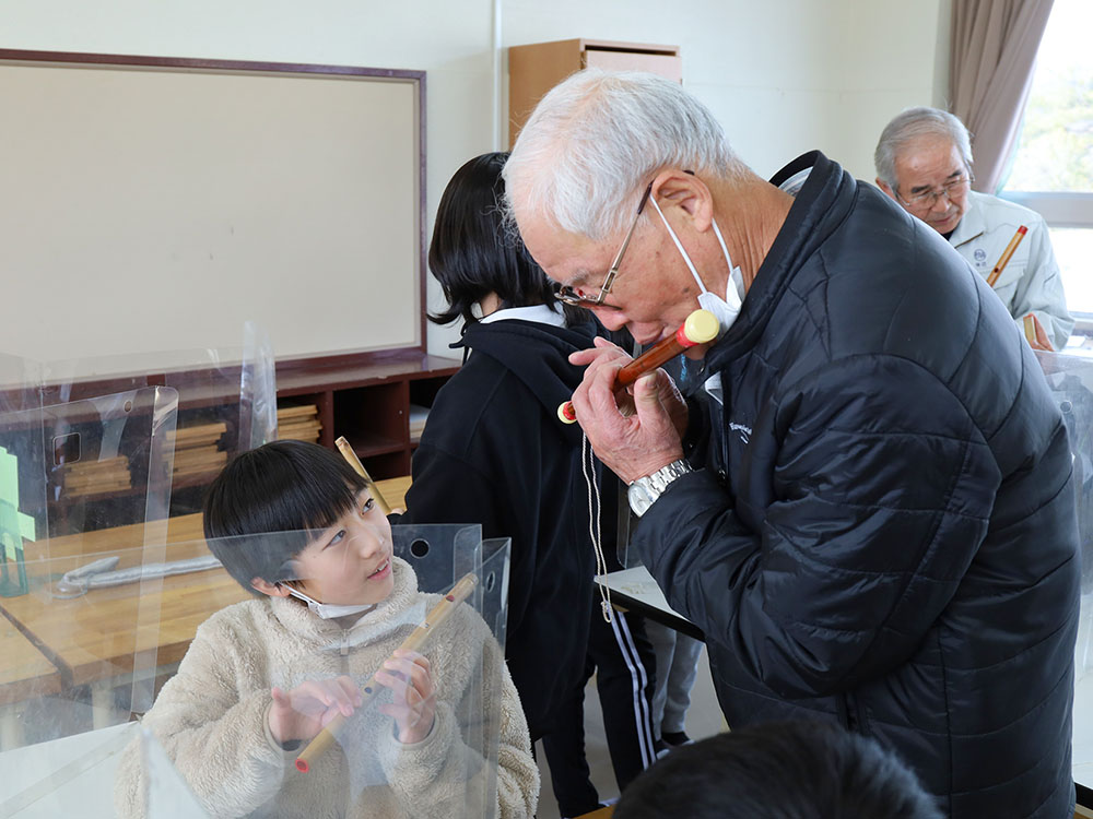 保存会の方から笛の演奏の指導を受ける児童