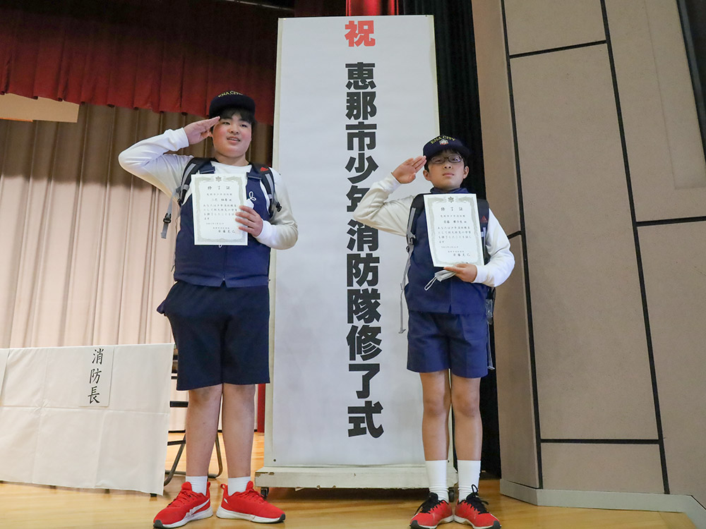 修了証を手に敬礼のポーズ