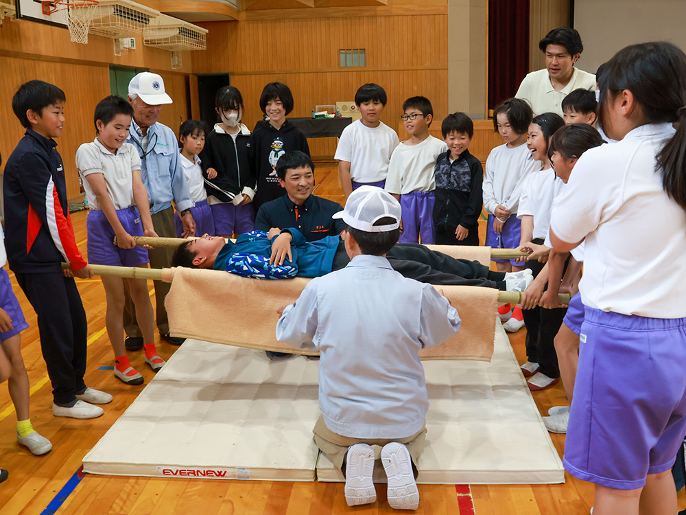 毛布を使って簡易担架を作り、体験する児童ら