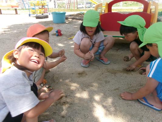 円になって座り砂遊びする5人の子どもたち