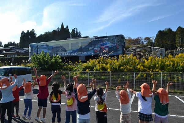RALLY JAPAN2023 と書かれたラッピングされた電車に手を降る数人の子どもたちの後ろ姿
