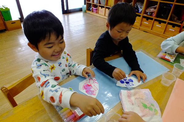 机に座り、笑顔でマジックでなにかを書いている二人の子ども
