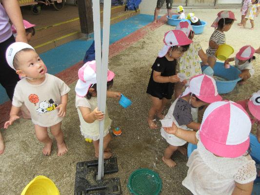 帽子をかぶった複数の園児が砂場で水遊びしている様子