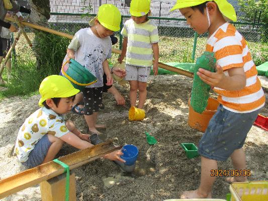晴れた日に木陰で砂遊びをする4人の子どもたち