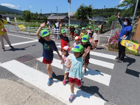 晴れた日に複数の子どもたちが手を上げて信号を渡っている様子