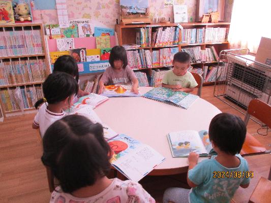 丸いテーブルに仲良く5人の子どもたちが座り、めいめいに絵本を読んでいる様子