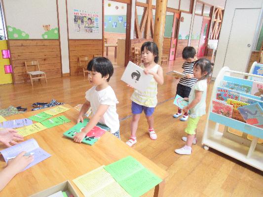 絵本を持つ4人の子どもたちが机越しに先生と話している様子