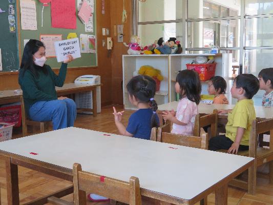 子どもたちが先生の前に座り、先生が英語の紙を提示している様子