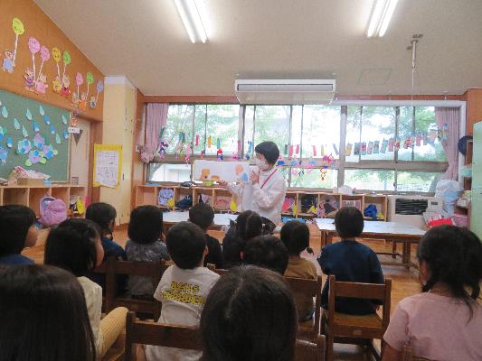 子どもたちが座って先生の紙芝居を見つめている後ろ姿